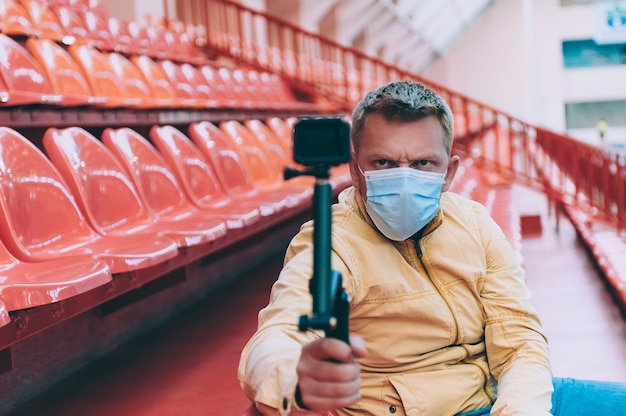 Blogger con máscara médica en el estadio graba video con cámara de acción.