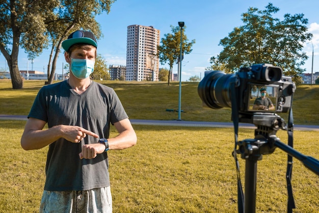 Un blogger con una máscara protectora graba un video en una cámara en el parque.