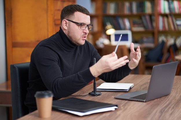 Blogger masculino que flui da biblioteca usando o laptop e microfone