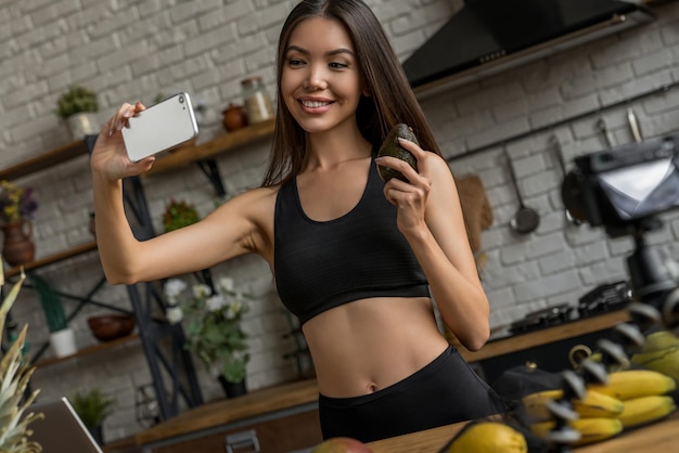 Blogger saludable mujer asiática haciendo selfie con aguacate frente a la cámara grabando vlog