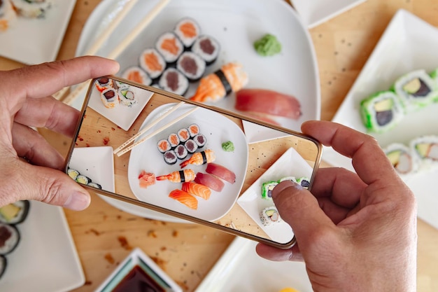 Blogger con teléfono móvil tomando fotos de delicioso sushi en la vista superior de la mesa