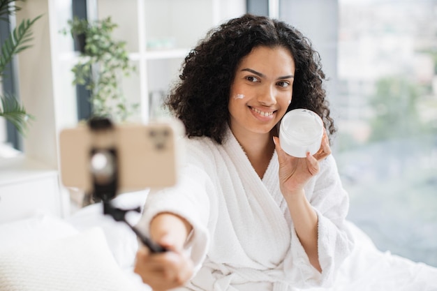 Foto una blogger tiene una clase de video en línea aplicando crema en su cara