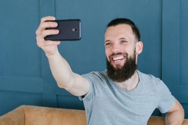 Blogger transmitiendo en vivo a través de un teléfono móvil. Hombre hipster barbudo que se comunica con los suscriptores a través de la cámara. nuevas ocupaciones modernas y formas de ganar dinero en línea concepto.