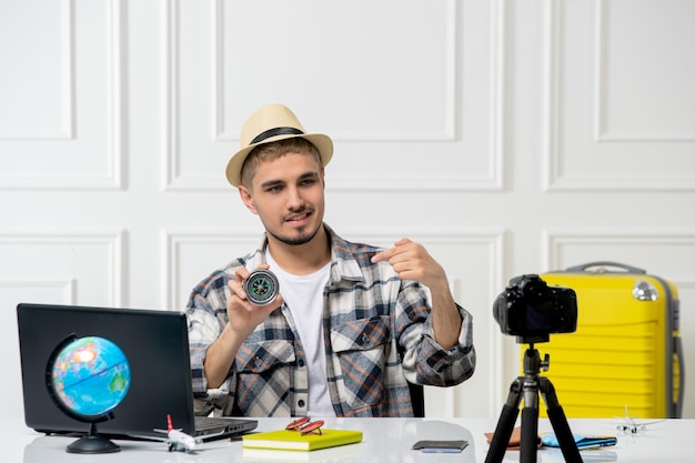 Blogger de viajes con sombrero de paja joven guapo grabando vlog de viaje en cámara mostrando brújula