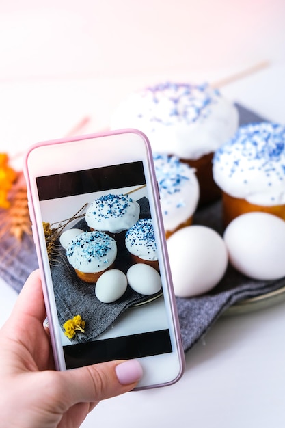 Blogger Vlogger Happy Day Páscoa brilhante Feriado de Páscoa Ortodoxa Tendência criativa e elegante Mão feminina tirando foto Bolo de páscoa caseiro e ovos Kulich Celular Minimalismo