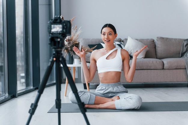 Bloggerin junge Frau mit schlanker Körperform in Sportbekleidung beim Yoga drinnen zu Hause