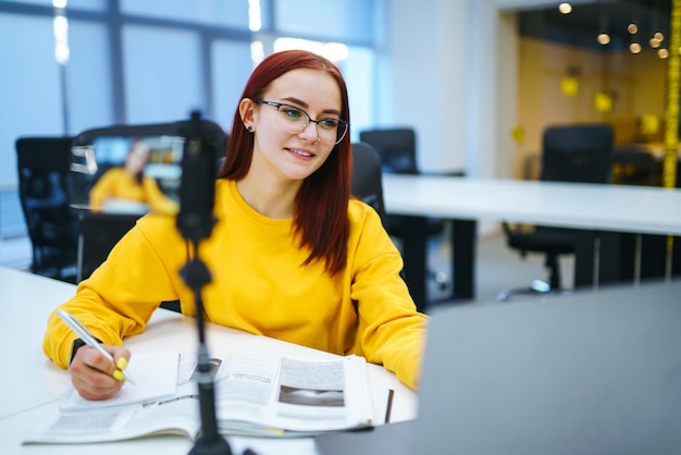 Bloggerin mit Laptop, die Videos aufzeichnet, während sie im Büro sitzt und über Startup-Unternehmen spricht