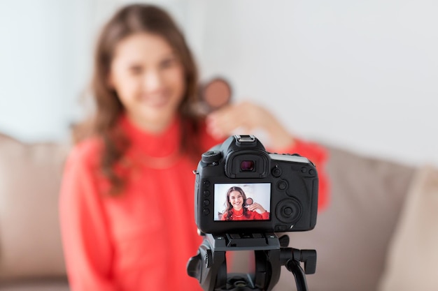 Blogging, tecnología, videoblog, maquillaje y concepto de personas: mujer sonriente feliz o bloguera de belleza con videotutorial de grabación de bronceador y cámara en casa