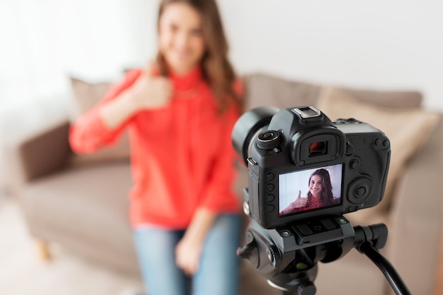 blogging, tecnologia, videoblog, mídia de massa e conceito de pessoas - mulher sorridente feliz ou blogueiro com câmera gravando vídeo e mostrando polegares para cima em casa