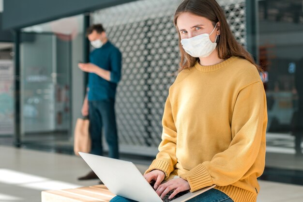 Blogueira com uma máscara protetora funciona em um laptop. conceito de proteção à saúde