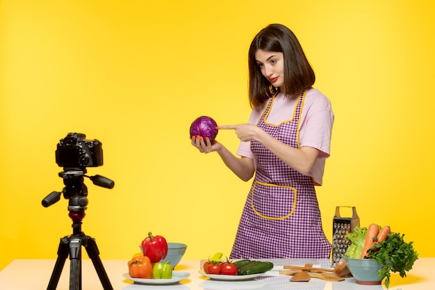 Blogueira de comida linda garota de avental rosa gravando vídeo para mídias sociais segurando uma cebola