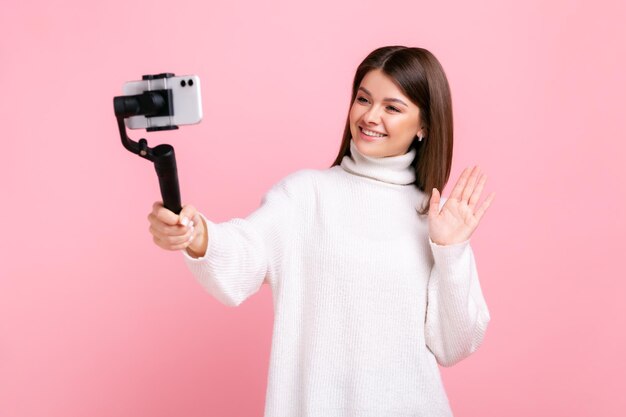 Blogueira feliz usando telefone inteligente e steadicam para transmitir seguidores de saudação de mão acenando