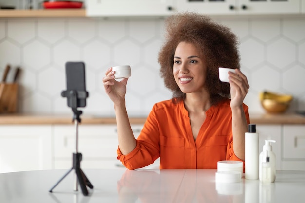 Blogueira negra gravando vídeo de revisão cosmética em casa com smartphone