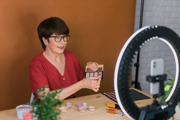 Blogueira ou influenciadora de beleza feminina de meia-idade com vídeo de gravação de produtos de maquiagem no quarto em casa u