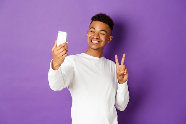 Blogueiro alegre, tirando selfie no smartphone, mostrando o símbolo da paz e sorrindo