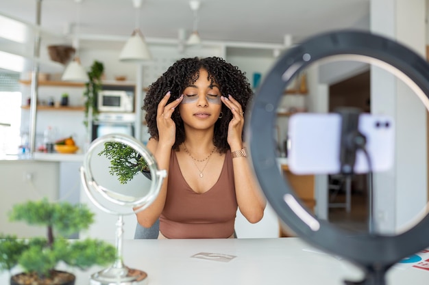 Foto blogueiro de beleza atraente mulher alegre gravando vídeo para seguidores testando e recomendando tapa-olhos mantendo vlog com dicas de maquiagem estúdio interno isolado em fundo rosa