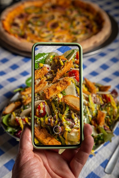 Blogueiro de comida usando um smartphone tirando fotos de uma salada leve em um restaurante italiano para compartilhar nas mídias sociais
