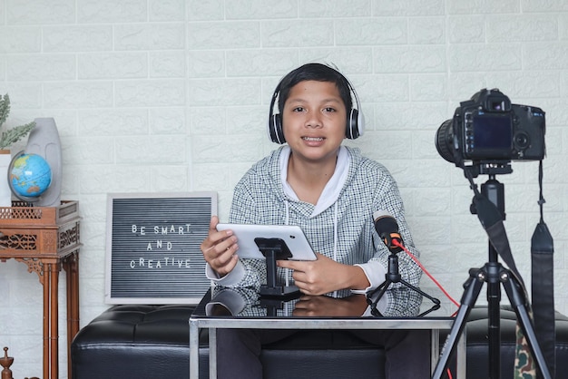 Blogueiro de criança asiática segurando tablet digital enquanto faz blog de vídeo. Influenciador online menino social med