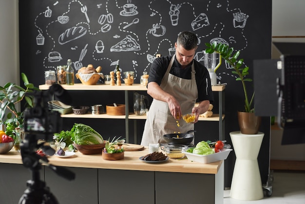 Blogueiro de culinária usando panela para cozinhar ele gravando vídeo para seu blog e cozinhando online na cozinha