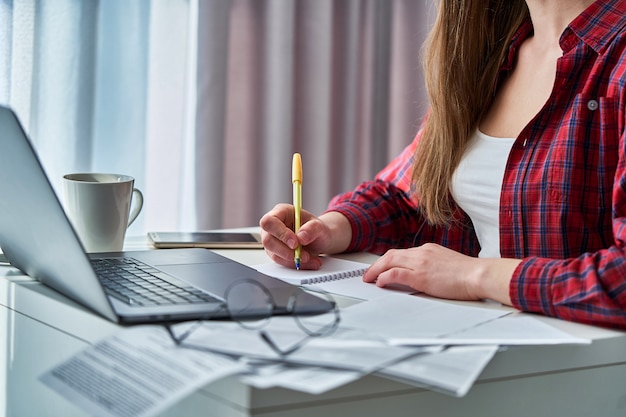 Blogueiro de mulher trabalhando remotamente no laptop e anotando informações importantes em laticínios para notebooks. mulheres durante educação a distância e cursos on-line aprendendo em casa