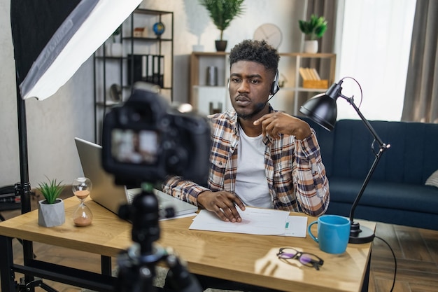 Blogueiro masculino africano em fone de ouvido gravando vídeo na câmera