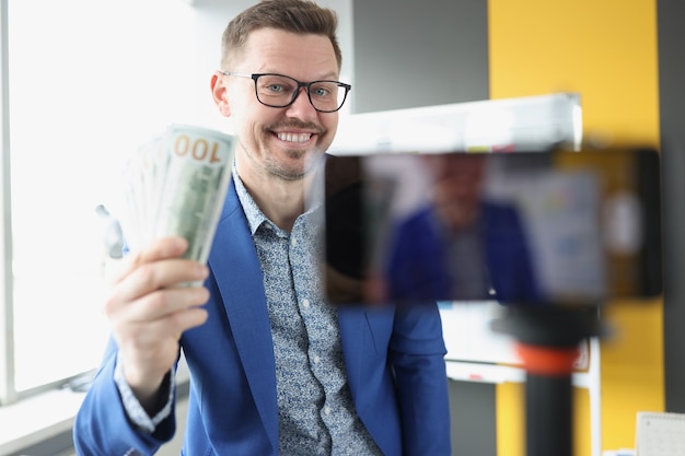 Blogueiro sorridente demonstra dinheiro em notas de cem dólares para a câmera. Ganhar dinheiro com um conceito de blog pessoal