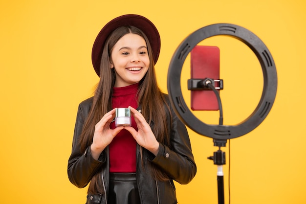 Una bloguera adolescente feliz usa una lámpara led selfie y un teléfono inteligente en un trípode para hacer un video tutorial en línea blog de belleza que presenta vlogging de cosméticos de maquillaje