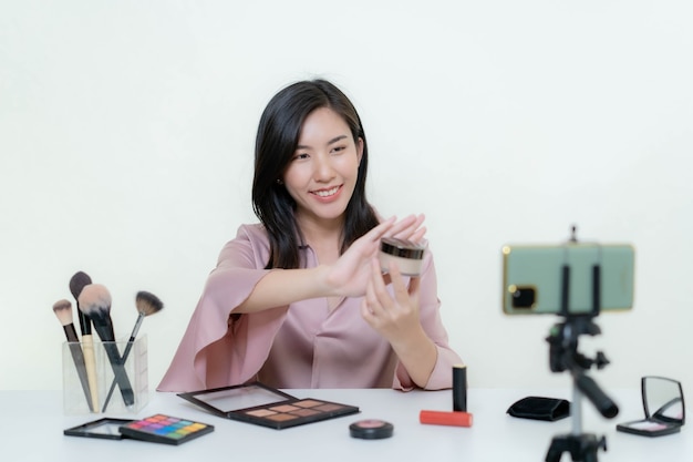 Una bloguera asiática bloguera de belleza grabando un video de ella con un lápiz labial naranja en un estudio.