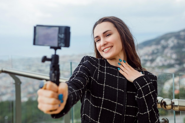 Una bloguera sonriente se está tomando una selfie sosteniendo su mano en el pecho contra el fondo de la vista de la ciudad