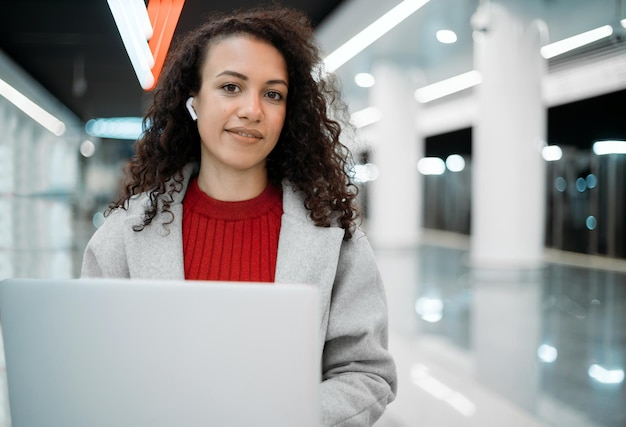 Bloguera sonriente con una laptop sentada en un banco en el metro