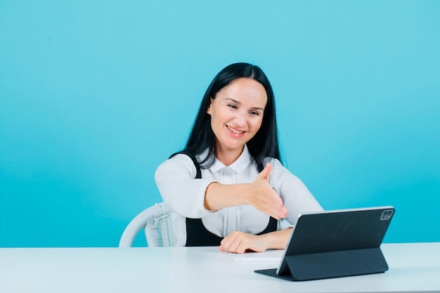 Una bloguera sonriente muestra un gesto de saludo extendiendo la mano a la cámara de la tableta con fondo azul