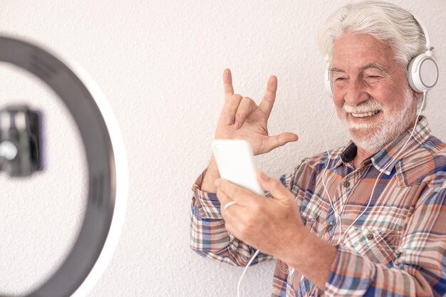 Bloguero senior con grabación de video durante una videollamada móvil. Pelo blanco y barba sonriendo viejo sobre fondo blanco.