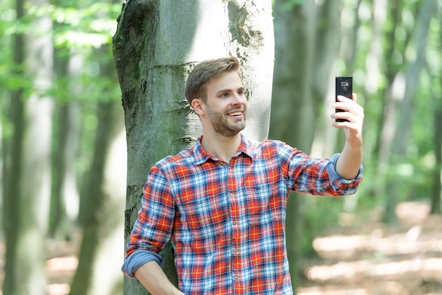 Un bloguero sonriente se toma una selfie en un smartphone foto de un bloguero se toma una selfie en el bosque