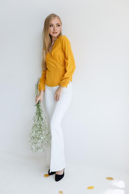 Blond in einem stilvollen modischen Bild mit trockenen Blumen an der weißen Wand. Herbst-Stylistin