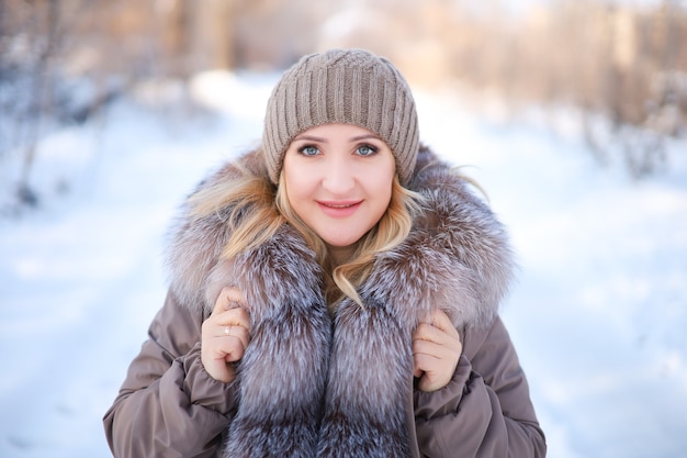 Blond in einer Jacke mit Pelzkragen und Hut auf der Straße im Winter