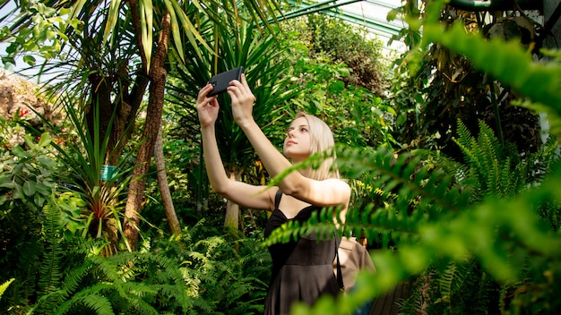 Blond mit Handy im Palmengewächshaus des Botanischen Gartens