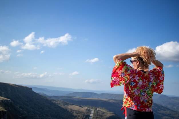 blonde Dame mit bedruckter Bluse und Sonnenbrille, die ihr Haar Rücken an Rücken hält