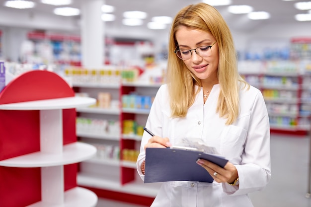 Blonde Drogistin in Uniform, die den Sortimentbestand in der Apotheke prüft