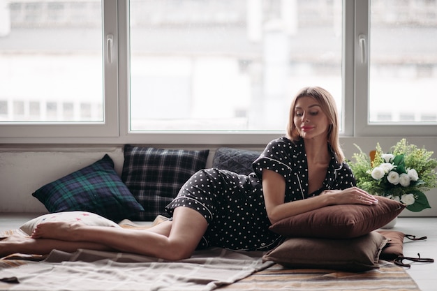 Blonde erwachsene Frau mit schönem Gesicht, die auf der Bettdecke sitzt und vor der Kamera posiert