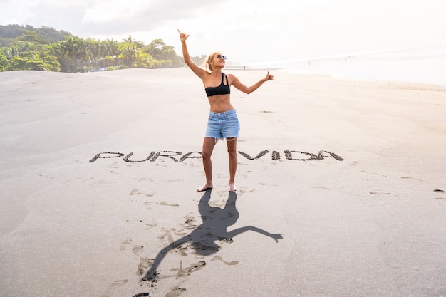 Blonde Frau am Strand mit Inschriften im Sand, die gestikulieren, glücklich zu sein