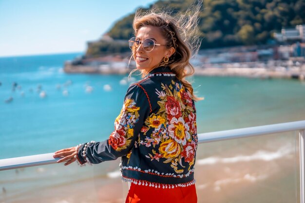 Blonde Frau auf einer Terrasse genießt die Sommerferien mit dem Meer im Hintergrund