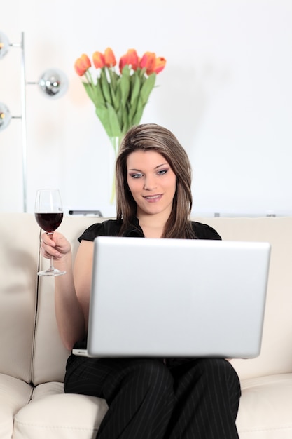 Blonde Frau auf Sofa mit Computer und Weinglas