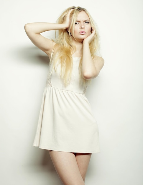 Blonde Frau der jungen Mode im weißen Kleid, das im Studio aufwirft