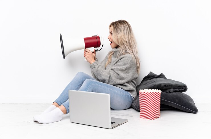 Foto blonde frau des teenagers, die popcorn isst, während sie einen film auf dem laptop sieht, der durch ein megaphon schreit