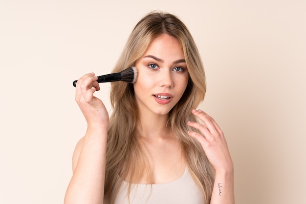 Blonde Frau des Teenagers mit Make-up-Pinsel über isolierter Wand