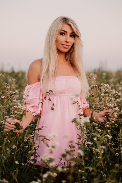 Blonde Frau des vertikalen Fotos, die im Sommerabend auf dem großen endlosen Feld der Gänseblümchen aufwirft.