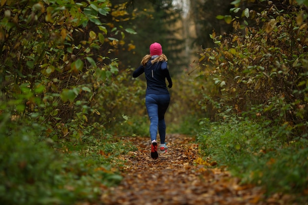 Blonde Frau, die auf der Spur im Herbstpark läuft