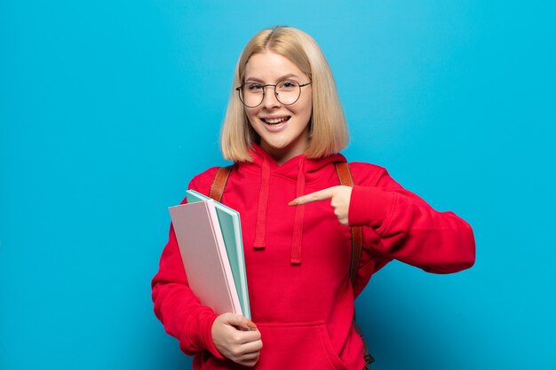 Blonde Frau, die aufgeregt und überrascht aussieht und zur Seite und nach oben zeigt, um Raum zu kopieren