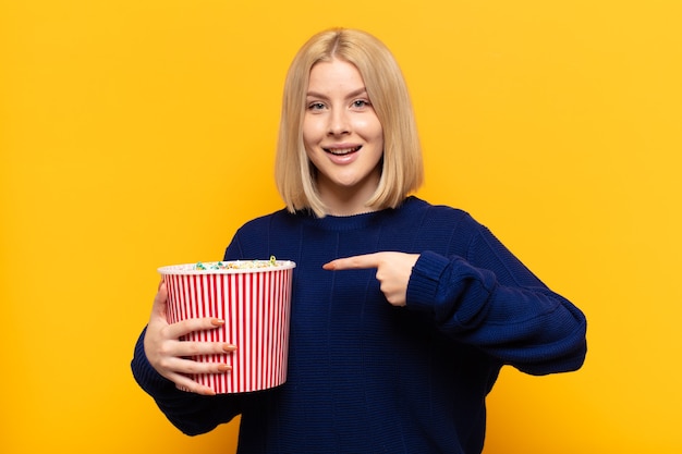 Blonde Frau, die aufgeregt und überrascht aussieht und zur Seite und nach oben zeigt, um Raum zu kopieren