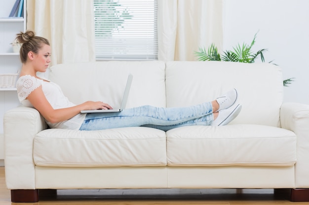 Blonde Frau, die den Laptop auf der Couch betrachtet